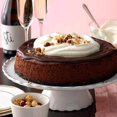 a chocolate cake with white frosting and nuts next to two champagne glasses on a table