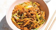 a white bowl filled with noodles and meat on top of a table next to chopsticks