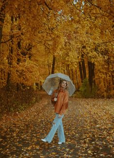 a woman is walking down the road with an umbrella in her hand and she has fallen leaves on the ground