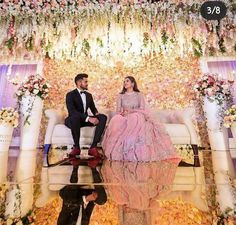 a man and woman sitting on top of a couch in front of a floral wall