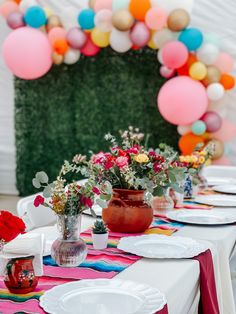 the table is set with plates and vases, flowers and balloons in the background