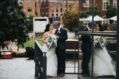 a bride and groom standing on a dock in front of some buildings with their reflection