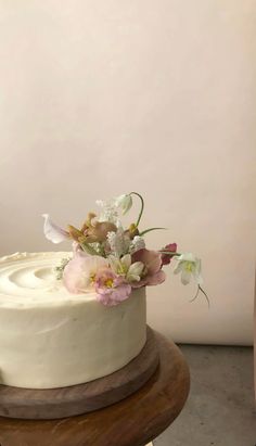 a white cake sitting on top of a wooden table next to a vase with flowers