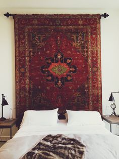 a large red rug hanging over a bed with white sheets and pillows on top of it