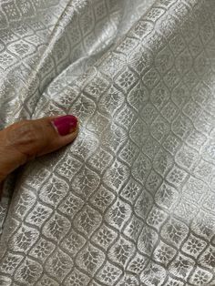 a woman's hand with red nail polish laying on a silver cloth covered bed