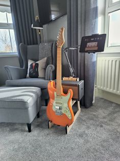 an orange guitar sitting on top of a wooden stand in front of a gray couch