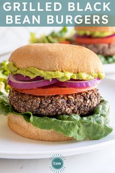 a hamburger with lettuce, tomato and onion on it sitting on a white plate