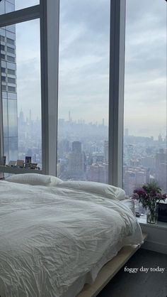 a bed in front of a window with the city skyline seen from it's bedroom