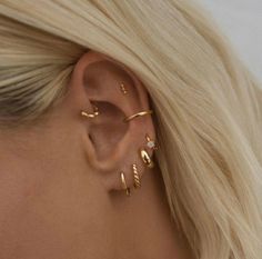 a woman with blonde hair wearing three gold ear cuffs and an earring that is shaped like a leaf