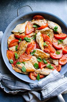 a pan filled with chicken, tomatoes and basil on top of a blue countertop