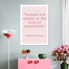 a pink cabinet and vase with flowers on it in front of a wall that says women are always at the front of revolution