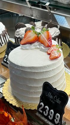 a cake with white frosting and strawberries on top in a display case at a bakery