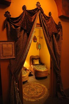 a room with a bed, chair and window in the corner that has drapes on it