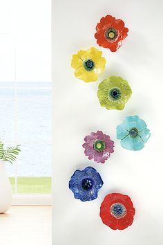 colorful glass flowers are hanging on the wall next to a vase with water in it