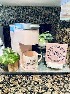 a coffee maker and two mugs sitting on a tray in front of a granite counter top