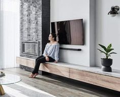 a woman is sitting on a ledge in the living room looking at the flat screen tv