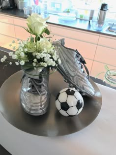 there is a vase with flowers and two soccer shoes on the table next to each other