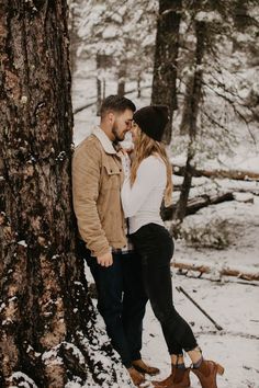 a man and woman standing next to each other near a tree in the snow,