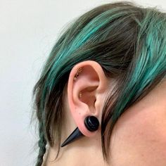 a woman with green hair and piercings on her ears is wearing an ear cuff