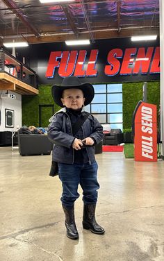 a small child wearing a cowboy hat and jeans standing in front of a full service sign