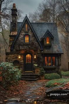 a stone house in the woods with lights on it's windows and steps leading up to