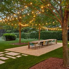 an outdoor dining area is lit up with string lights and trees in the back yard