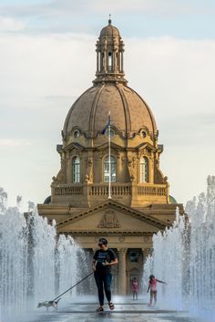 a woman is using a mop in front of a building with water spouting from it