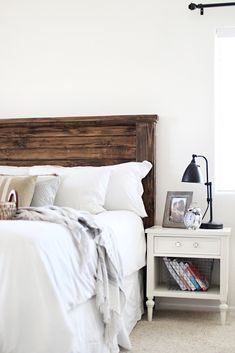 a bed with white sheets and pillows next to a night stand on the end table