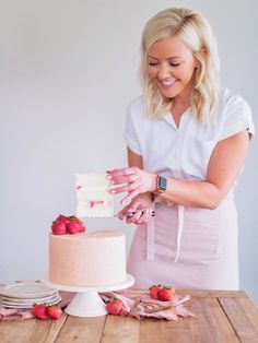 a woman is cutting into a cake with strawberries on the table