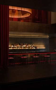 a dimly lit bar with red curtains and stools