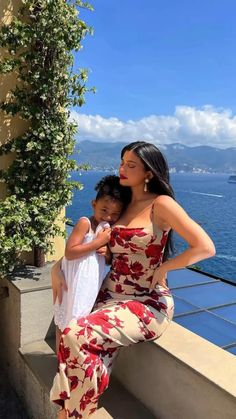 a woman and child are posing for a photo on the balcony overlooking the ocean in matching outfits