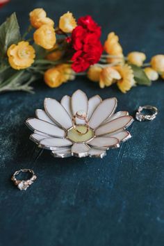 a white flower brooch sitting on top of a table next to some yellow and red flowers