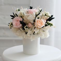 a white vase filled with lots of pink and white flowers on top of a table