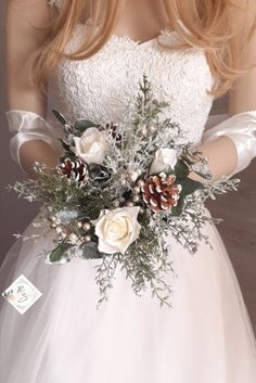 a woman in a white wedding dress holding a flower bouquet with pine cones and flowers