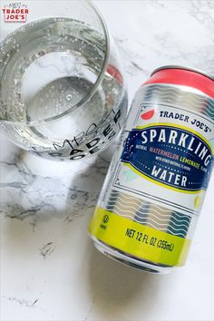 a can of sparkling water next to a glass on a marble counter top with a measuring tape