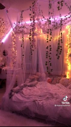 an unmade bed with lights strung from the ceiling and curtains hanging down over it