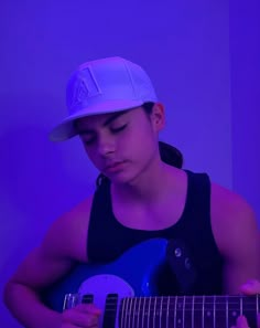 a young man wearing a baseball cap playing an acoustic guitar in front of a purple background