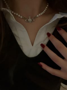 a close up of a person wearing a necklace and holding her hand on her chest