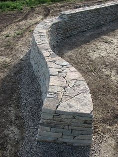 a stone wall in the middle of a field with grass and dirt around it,