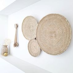 three woven baskets hanging on the wall next to a vase with flowers and a brush