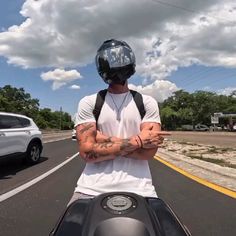 a man with tattoos on his arms riding a motorcycle down the road in front of a car