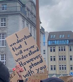 a person holding a sign in front of a building with words written on it and people standing around