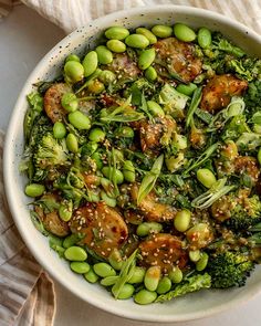 a white bowl filled with broccoli, peas and other vegetables on top of a table