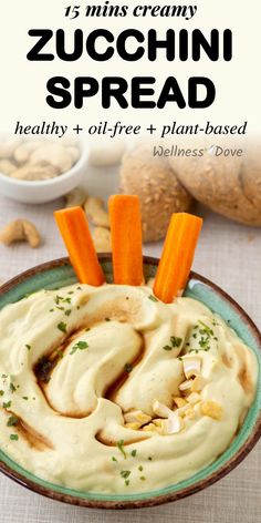 a bowl filled with hummus, carrots and cashews next to bread