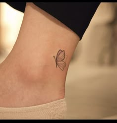 a small butterfly tattoo on the side of a woman's ankle, with black ink