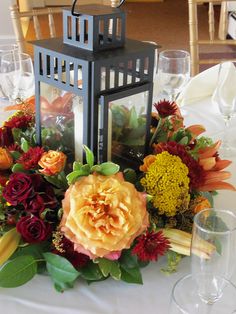 an arrangement of flowers and greenery on a table with a lantern at the center