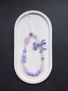 a purple and white beaded bracelet on a tray with a pink butterfly charm hanging from it