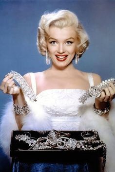 a woman in a white dress and fur stoler holding up some silver bracelets