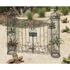 an iron garden gate with plants growing out of it's sides in a gravel area