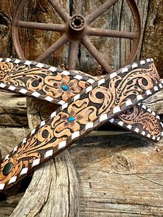 a pair of brown and white leather belts on top of a wooden table next to a wagon wheel